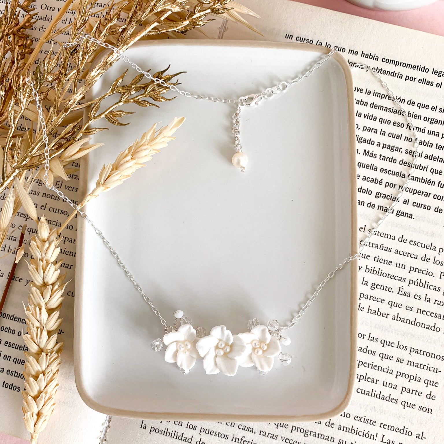 A white floral necklace displayed on a plate with dried wheat and a text document in the background, presented as a potential accessory for brides.