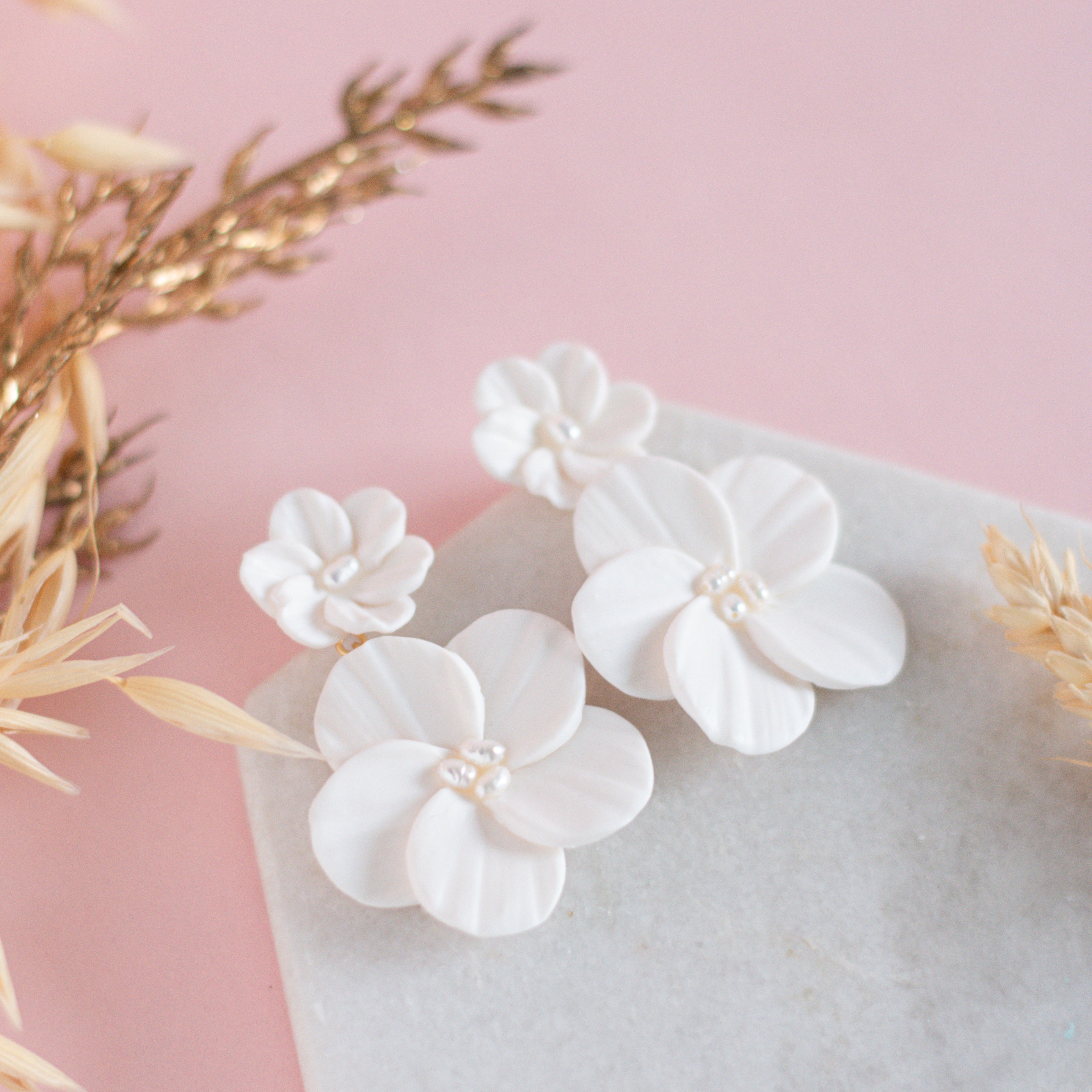 White floral earrings on a light pink surface with gold leaves.