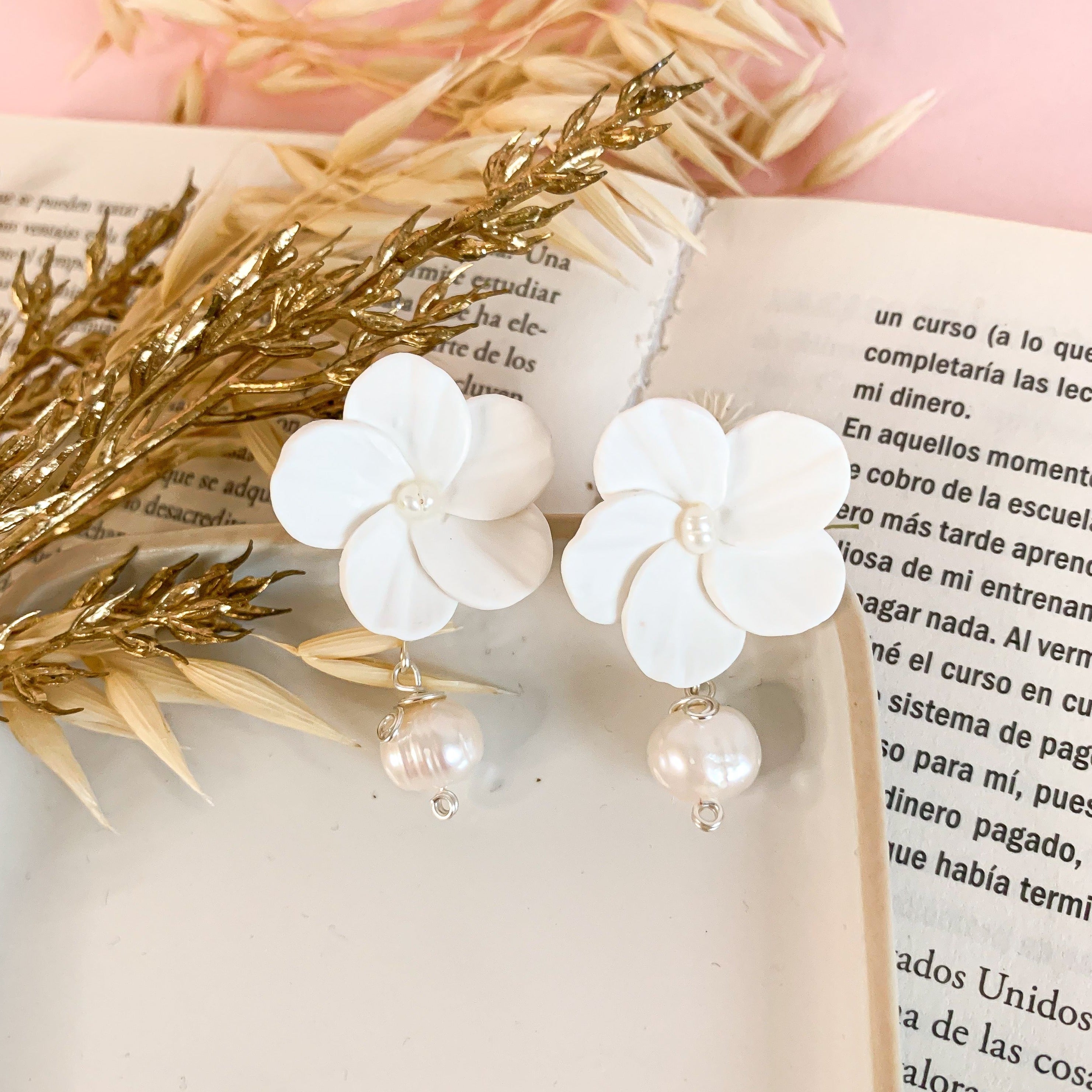 A pair of white flower earrings with gold accents and pearl drops