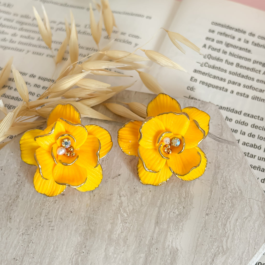 Yellow flower earrings on an open book with a pink background