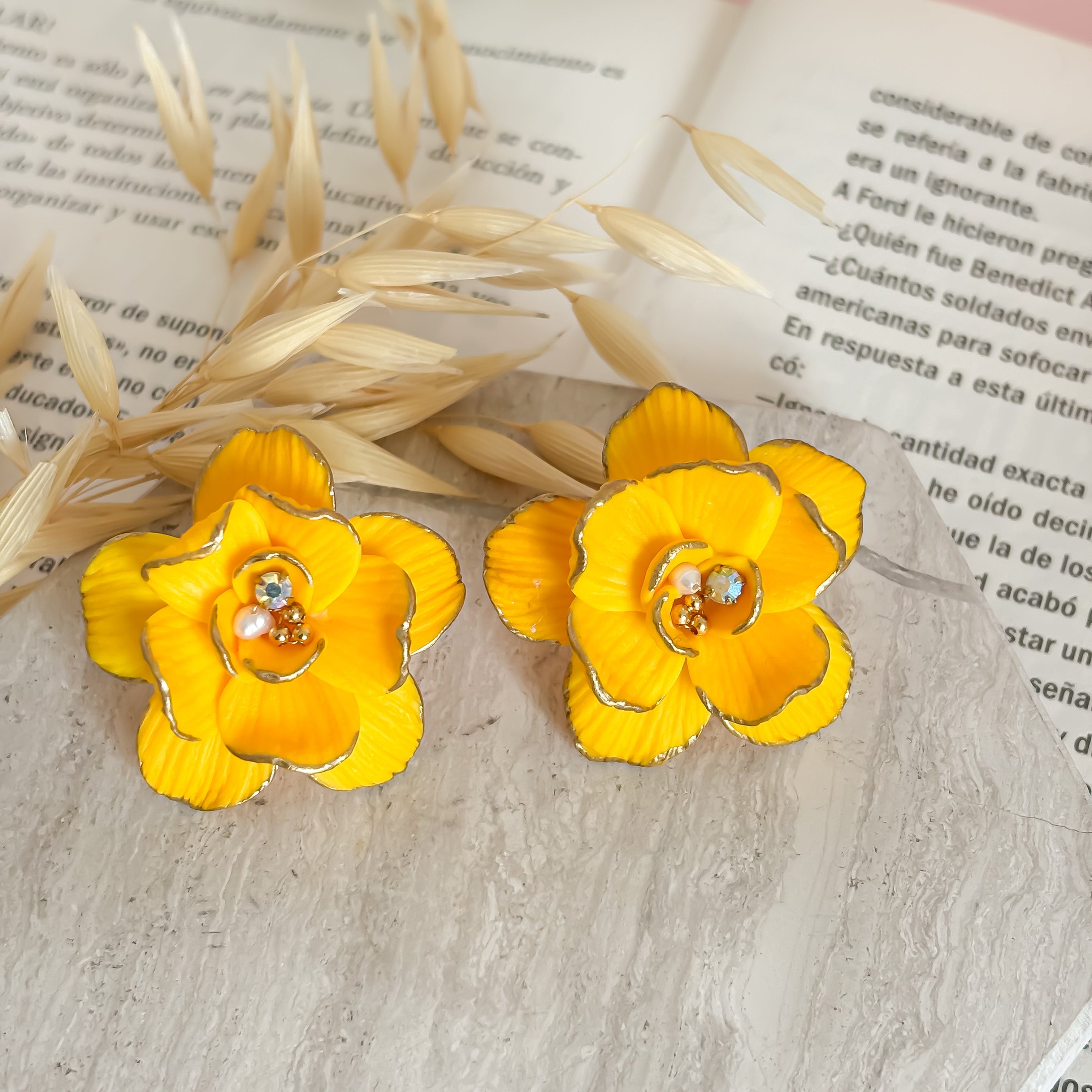 Yellow flower earrings on an open book with a pink background
