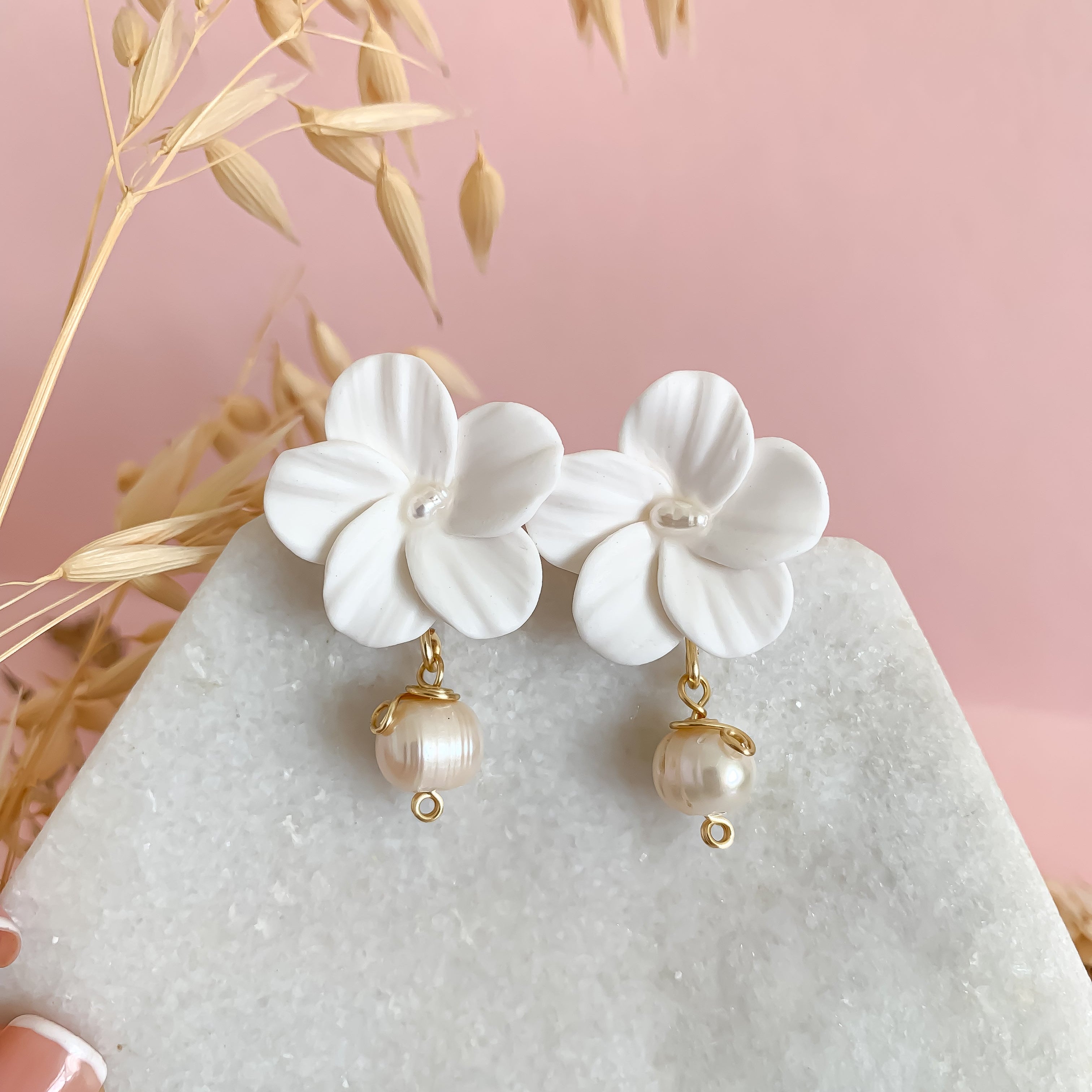 White floral earrings with pearl drops on a light pink background