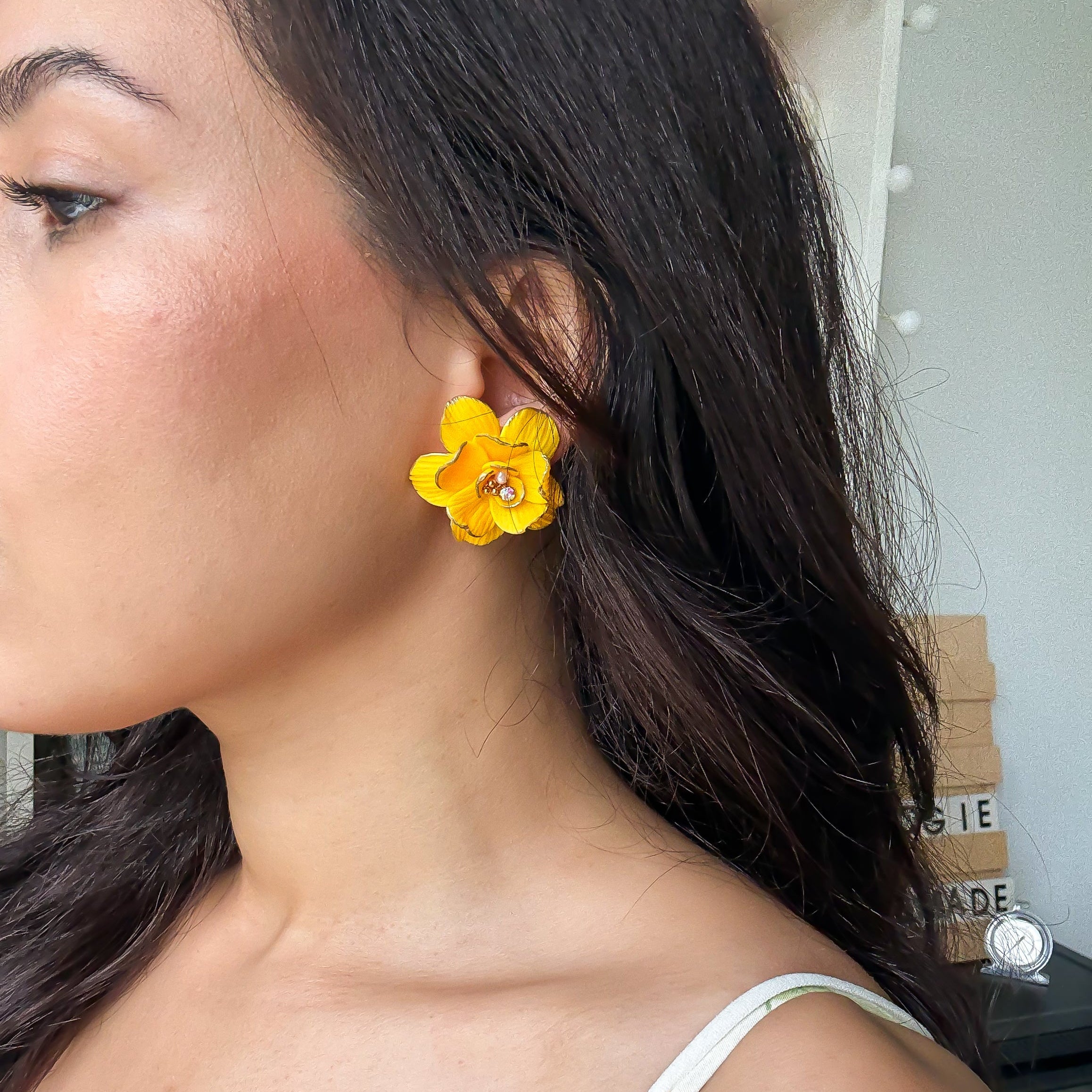 Close-up of a person wearing yellow floral earrings with a neutral background.